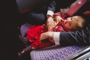 A small child in a red dress and pink jacket is leaning against an adult wearing a suit with a pink tie, perhaps captured by one of those talented Bristol wedding photographers. The child holds a pacifier and a small container, sitting on a colorful, patterned seat.