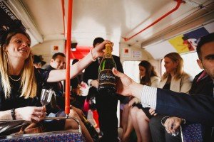 Inside a bus brimming with celebratory energy, people in formal attire share a bottle of Lanson champagne. Wine glasses clink as laughter fills the air, capturing candid moments reminiscent of those beautifully documented by wedding photographers in Bristol. .