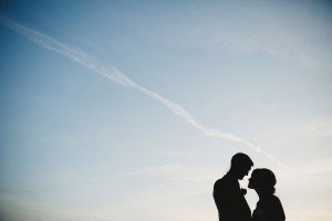 Silhouette of a couple facing each other against a clear blue sky with a wispy white cloud above them, captured by Somerset wedding photographers. The scene conveys a romantic and serene atmosphere ideal for documentary wedding photographers.