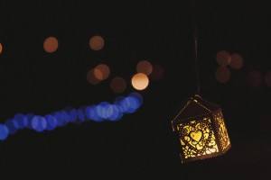A decorative lantern with intricate patterns glows warmly against a dark background. Soft, out-of-focus lights in shades of blue and orange create a bokeh effect, adding a dreamy atmosphere—perfect inspiration for Somerset wedding photographers capturing magical moments.