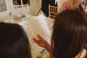 Two people seated at a table are looking at an open menu card in a dimly lit restaurant. The table is set with wine glasses, cutlery, and a chair with a pink bow visible in the background, creating the perfect ambiance for Bristol wedding photographers to capture intimate moments.
.