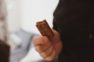 A person holds a partially eaten chocolate Bourbon biscuit, its surface embossed with Bourbon and dotted with holes. The background is softly blurred, much like the artful compositions crafted by wedding photographers Somerset, drawing your eyes to the tasty treat in hand.