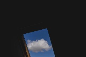 A fluffy white cloud is visible through a skylight against a clear blue sky. The rest of the image is dark, highlighting the window and sky—much like how wedding photographers Bristol expertly capture intimate moments against striking backdrops.