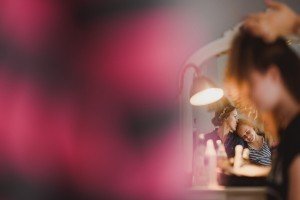 A woman and a young girl are smiling at each other in front of a mirror. The scene is blurred by a pink foreground, creating a warm and intimate atmosphere, reminiscent of the heartfelt moments expertly captured by documentary wedding photographers.