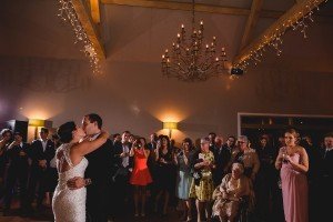 A couple shares a dance at their wedding reception, captured beautifully by Somerset wedding photographers. Surrounded by guests smiling under the chandeliers warm glow, some hold drinks while a woman in pink stands nearby, the perfect scene of love and joy preserved forever.