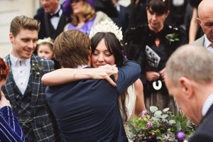 A bride in a white dress and tiara hugs a man in a suit amid the joyful atmosphere captured by talented wedding photographers from Bristol. Surrounded by formally dressed guests, she holds a bouquet in her left hand, embodying the celebratory spirit of the day.