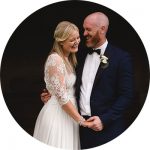 A bride and groom are happily holding hands and laughing, captured perfectly by talented Somerset wedding photographers. The bride shines in a lace dress, while the groom dons a dark suit with a bow tie and boutonniere. They stand close together, framed against a moody backdrop.