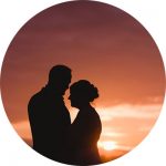 A silhouette of a couple faces each other with a sunset backdrop. The skys gradient of orange and purple hues creates a romantic and serene atmosphere, perfect for capturing by talented Bristol wedding photographers.