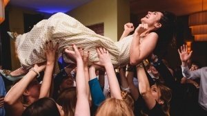 A woman in a white dress is joyfully lifted above a crowd at a lively event, her laughter echoed by the cheers and smiles around her. Captured beautifully by documentary wedding photographers, this unforgettable moment highlights the exuberance that wedding photographers in Bristol bring to life.